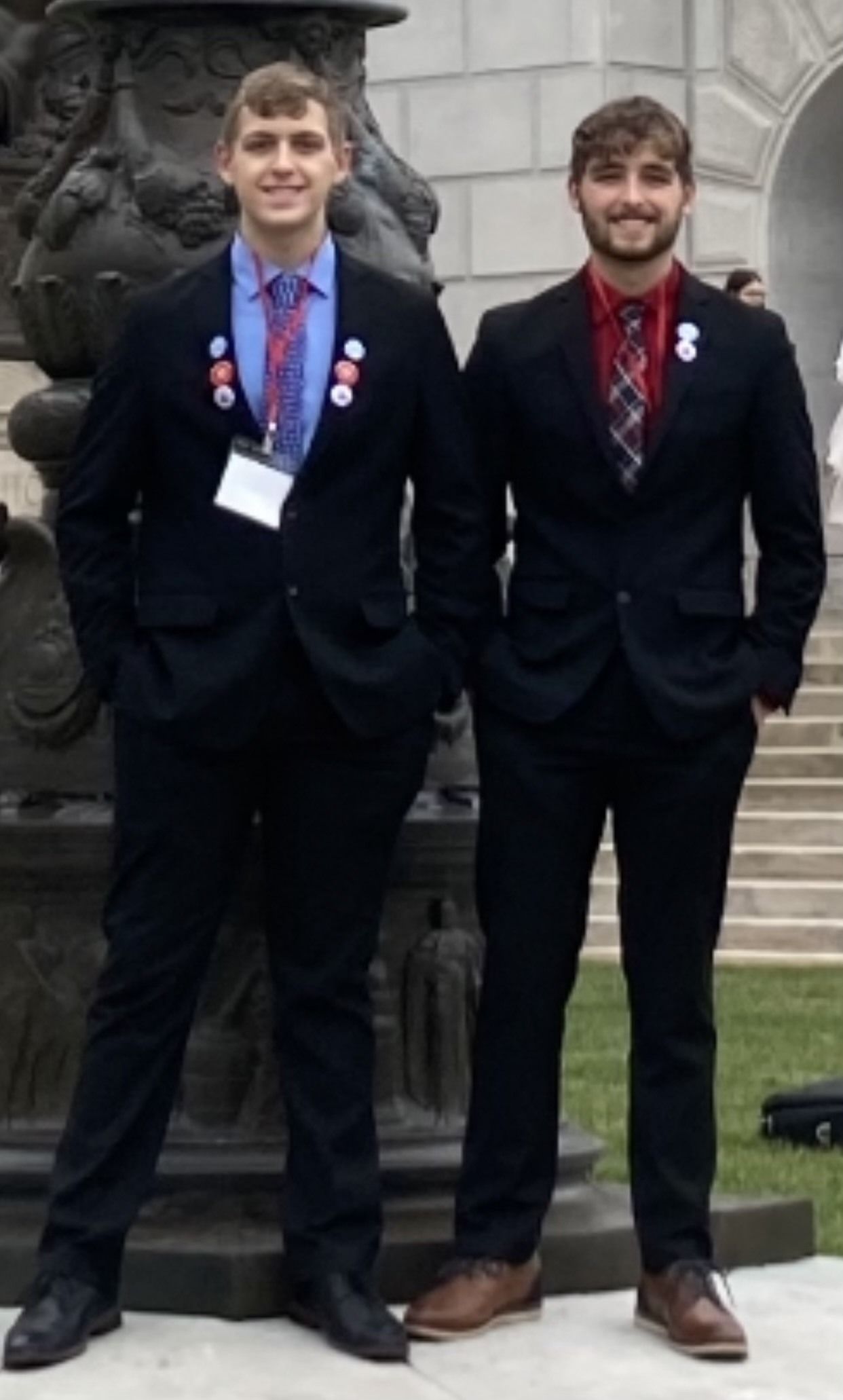 Will and Cole Bastean posted in suits, in front large statue and staircase.